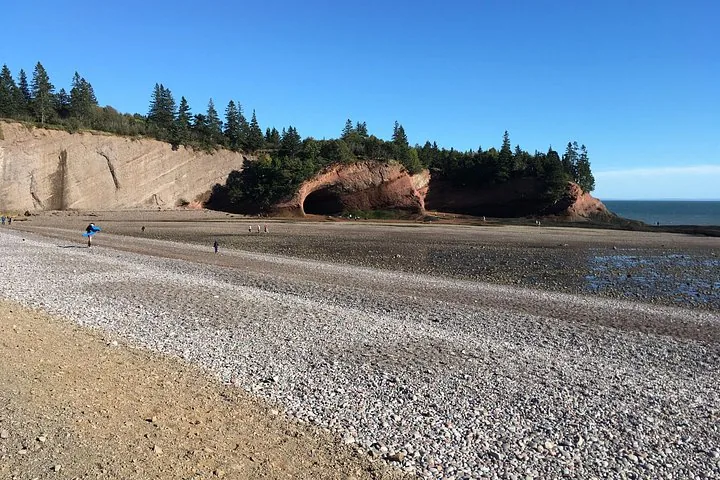 Ampia veduta di una spiaggia di ciottoli che conduce a scogliere di arenaria rossa con grotte marine.