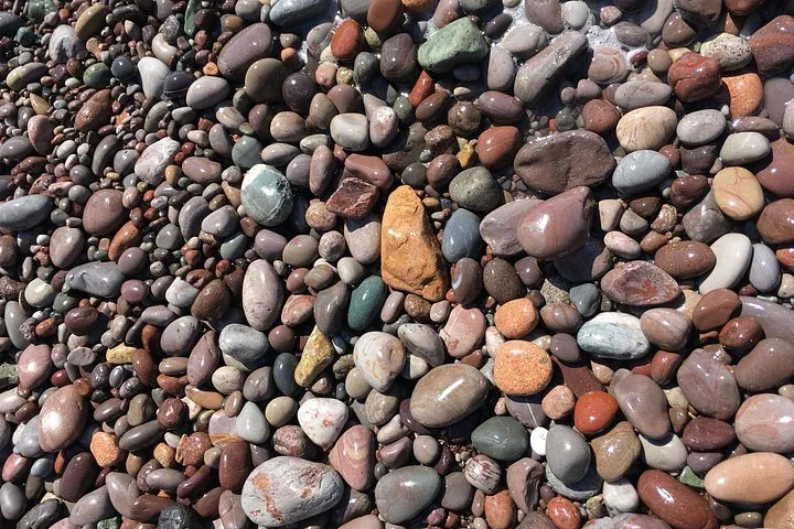 Close-up of wet, smooth, colorful pebbles and rocks on a beach surface.